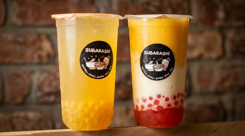 Two Subarashi boba drinks, one yellow with clear boba, the other layered yellow, white, and red with red boba.