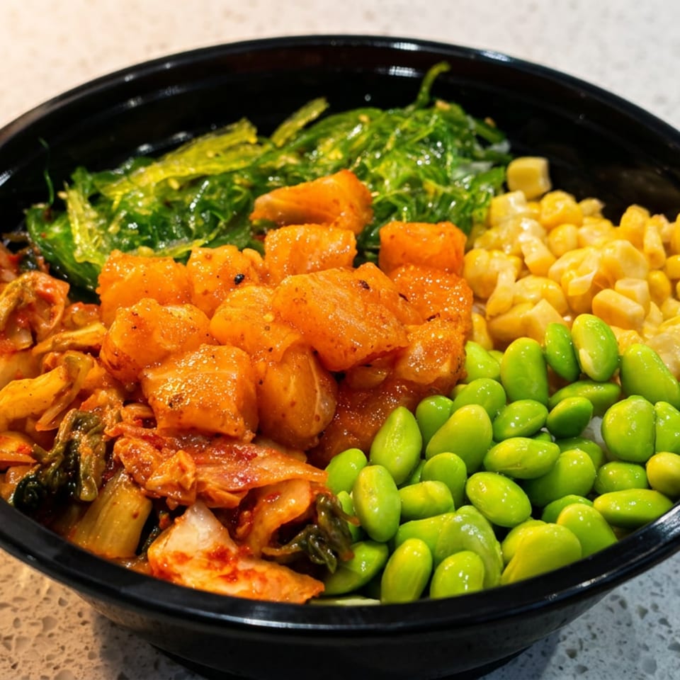A fresh poke bowl filled with diced salmon, kimchi, seaweed salad, corn, and edamame.