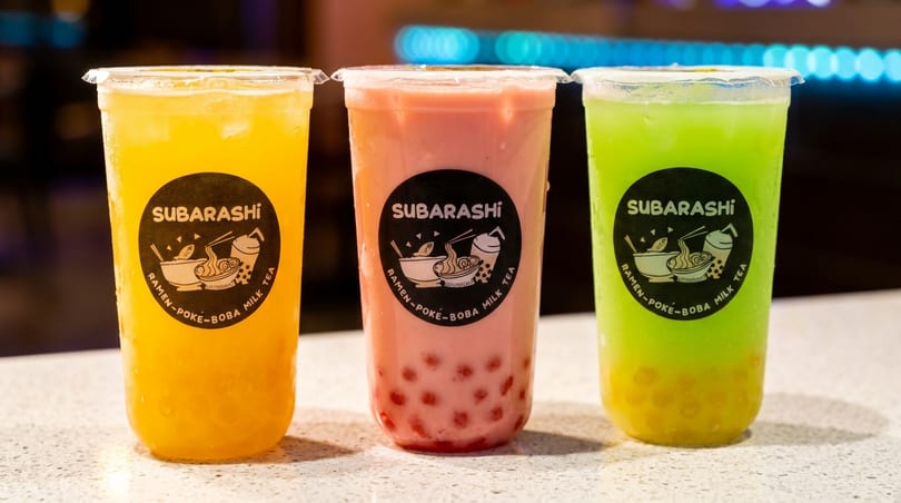 Three Subarashi boba teas: yellow, pink with red pearls, and green with yellow pearls.