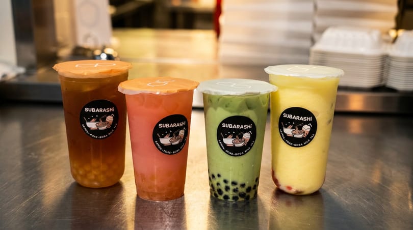 Four colorful Subarashi bubble tea drinks with various toppings on a metal counter.