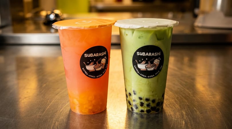 Two Subarashi boba milk teas, one orange and one green with tapioca pearls.